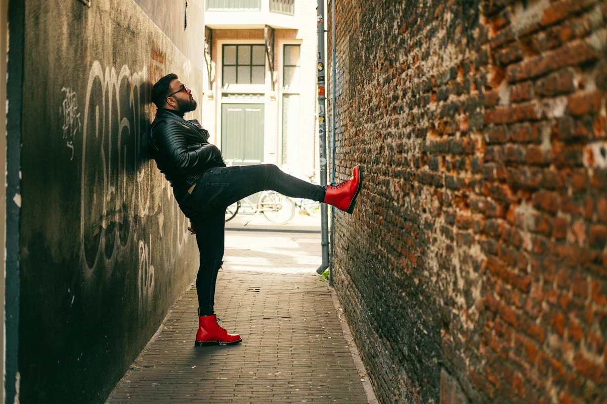 Man in a black leather biker jacket leaning on a brick wall