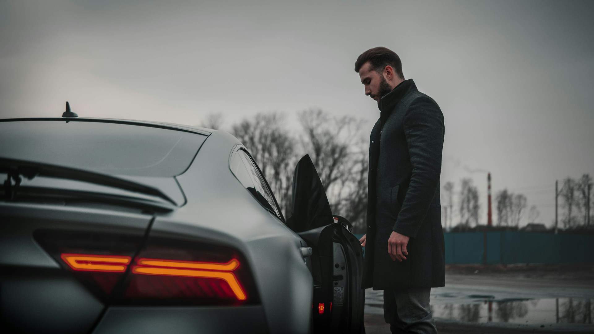 Man in a premium black coat beside a luxury sports car