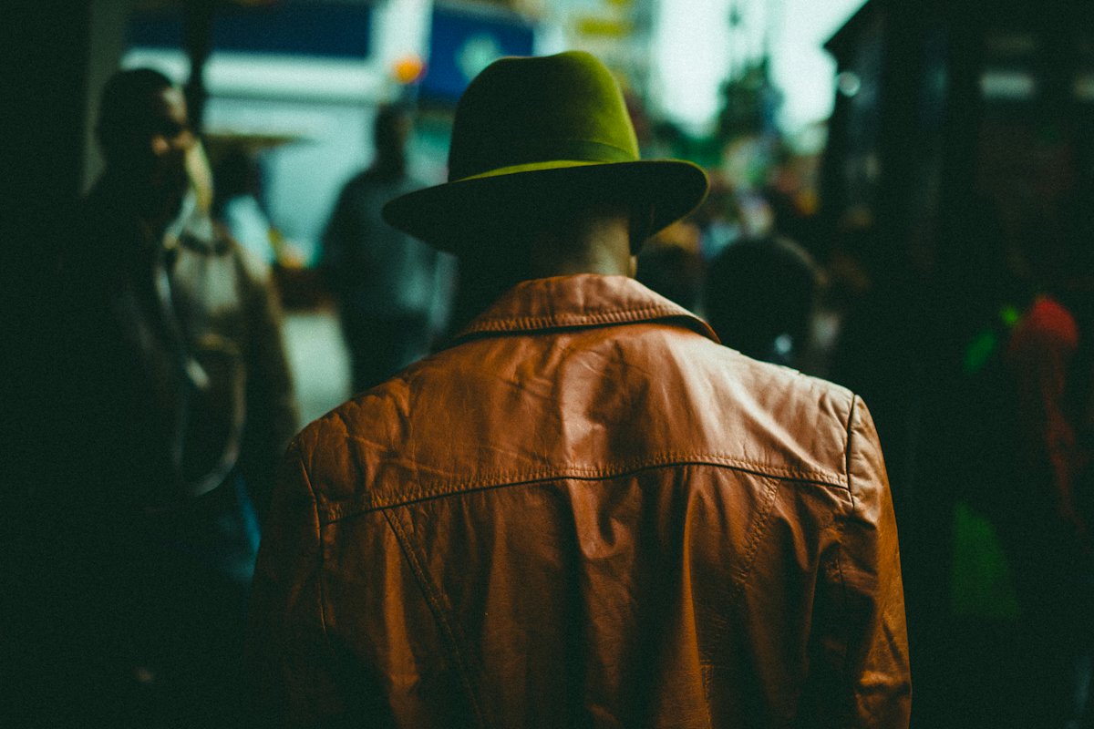 Man in a tan leather jacket and hat seen from behind